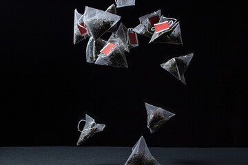 Pyramid tea bags on black background. Fast brewing tea. Many tea bags fall down.