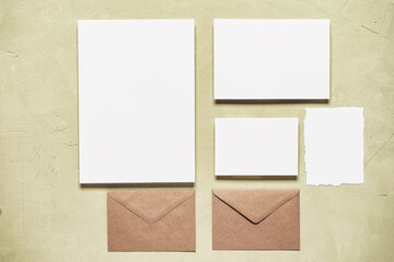 Blank paper white cards mockup and brown craft envelope on beige concrete background. Modern stationery still life. Template for your design. Top view, flat lay.