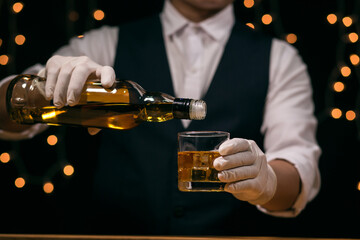 Waitress man standing pours whiskey into a glass 