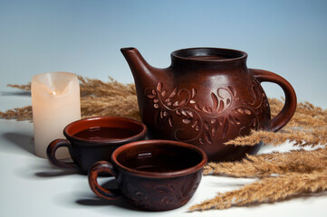 Clay teapot and cups of tea, white candle and dry herb