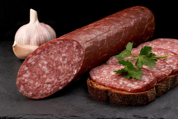 Raw smoked sausage and garlic sandwich on a black slate board. Close-up.