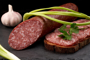 Side view of raw smoked sausage and a sandwich made from it with herbs and onions. Close-up.