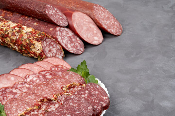 Set of jerky and uncooked smoked sausage whole and slices on a gray background, side view with copy space.