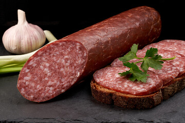 Side view of raw smoked sausage and a sandwich made from it with herbs and onions. Close-up.