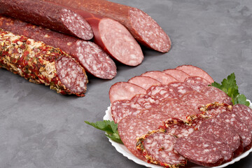 Set of jerky and uncooked smoked sausage whole and slices on a gray background, side view with copy space.