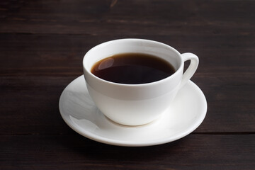 Black strong espresso coffee in a white ceramic cup. Wooden dark background, copy space.