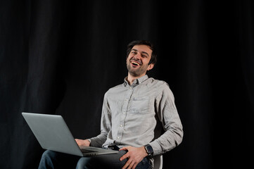 Pleasant positive business man using laptop.Happy smiling man in shirt works on laptop on a dark background