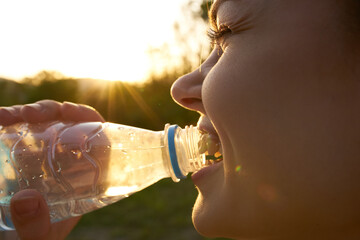 woman drinks water from a plastic bottle in summer outdoors