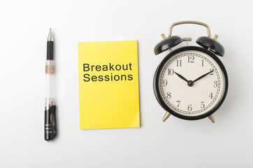Top view of a alarm clock and pen with written Breakout Sessions on white background. Selective focus.