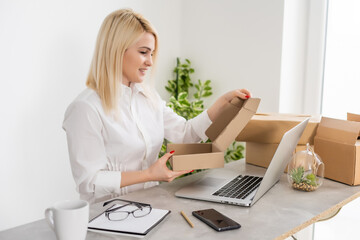 Young woman sitting at table, opening postal packet, smiling, box