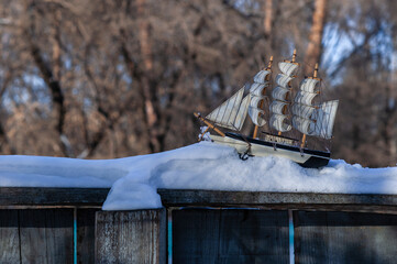 Model of a sailboat in the snow on a wooden fence