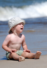 Craing little boy sitting on the beach