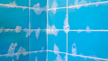 Bathroom shower blue tiles with lather suds soap foam after shower closeup selective focus background