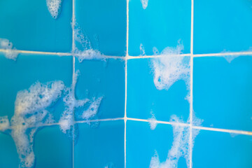 Soap foam lather closeup on bathroom shower blue tiles after shower selective focus background