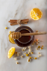 Glass jar full of honey and dipper with dried camomile herb tea, lemon and cinnamon sticks. Herbal supplements concept. 