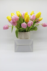 bouquet of pink and yellow tulips in a white vase,  envelope nearby