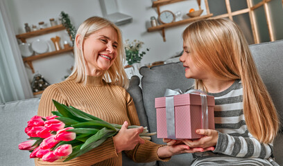 This gift is for you my loving grandmother! A little girl gives her grandmother a gift with a bouquet of pink tulips. Concept of family, spring day, mother, birthday, generation, love.