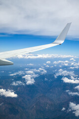 An airplane wing over Akaishi Mountains, aerial view form a passenger seat. Clouds and mountains covered with snow below.