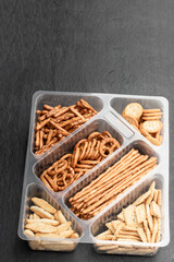 Crunchy mix of pretzels and crackers with sesame and poppy seeds on black stone background