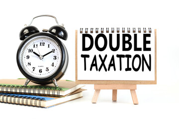 doble taxation. text on white notepad paper on a stand next to our desk clock on a sideboard. on white background