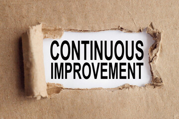 CONTINUOUS IMPROVEMENT. text on white paper over torn paper background.