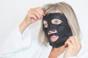 Senior woman applies black cosmetic mask to her face. Anti age concept. Mature woman face after spa treatment. Beauty spa treatment. Plastic surgery clinic, cosmetology, new senior