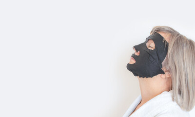 Senior woman profile, applies a black cosmetic mask to face. Anti age concept. Mature woman face after spa treatment. Beauty spa treatment. Place for text