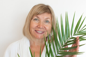 Fototapeta premium Senior woman smiling Anti-aging concept with palm leaf. Mature woma face after spa treatment. Old age in joy, plastic surgery clinic, cutie grandmother, cosmetology, new senior