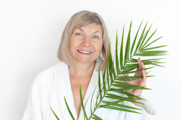 Fototapeta premium Senior woman smiling Anti-aging concept with palm leaf. Mature woma face after spa treatment. Old age in joy, plastic surgery clinic, cutie grandmother, cosmetology, new senior
