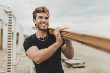 Young builder carries wooden planks on his shoulder