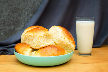 A bun and a glass of milk on a wooden table. Pie and a glass of milk on a gray background.