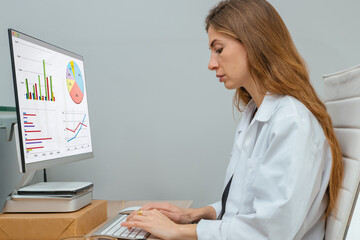 Young female doctor in the hospital, works and analyzes the statistics of the sick on the computer.