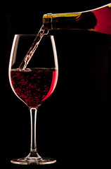 Naklejka na ściany i meble Pouring a glass of red wine on black background.