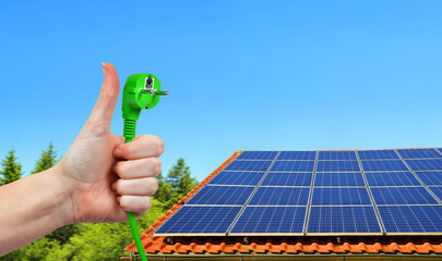 Solar energy panel on the roof of the house and hand holding green electric plug in sunny day....