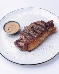 Delicious beef steak with sauce served on a white plate over white background. BBQ meat, barbecue concept.