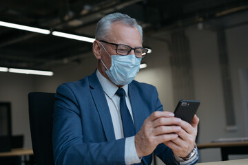 Senior man in medical mask using mobile phone, communication, searching online, working from home. Coronavirus, social distance, stay at home concept