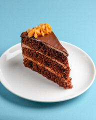 Piece of chocolate cake with icing on blue background. Sweet dessert for tea or coffee time.