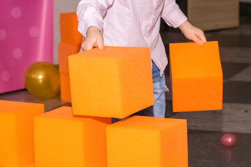 large orange blocks of paralon in the children's center. the child builds a wall from soft cubes. close-up - obrazy, fototapety, plakaty