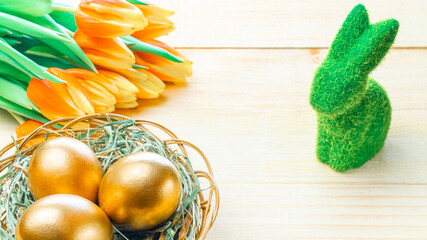 Easter eggs gold. Golden colour egg in basket with spring tulips, white feathers on wooden background in Happy Easter decoration. Congratulatory easter design.