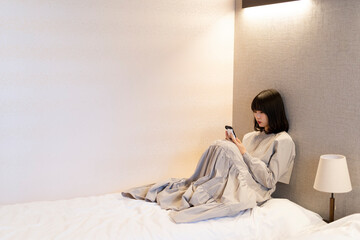 寝室でスマートフォンを使う女性