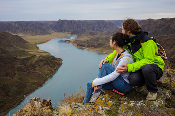 Young couple outdoors near the beautiful river canyon. Young people are resting on the edge of the cliff. Spring landscape. The Ili River. Kazakhstan
