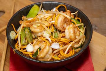 A delicious Chilli Bean King Prawn Noodles with chop sticks along side the bowl on a wooden chopping board