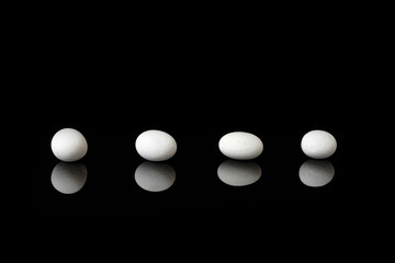 White sea pebbles on black background with mirror reflection.