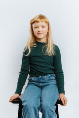 portrait of cute blonde girl sitting on chair against white background