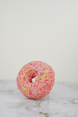 Pink donut on yellow background. Icing sugar sweet food. Colorful snack dessert. Glazed sprinkles. Enjoy a delicious pastry breakfast. Bakery cake. Donut with glaze