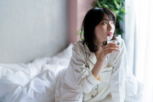 ベッドで水を飲むパジャマの
女性