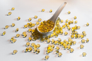 Spoon with yellow oil-based capsules and a scattering of pills around. Light background.