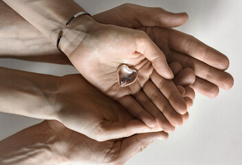 Women's hands hold a glass heart, men's hands support women's hands.