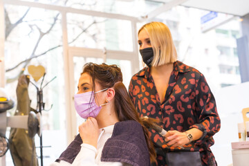 Young hairdresser with face protection mask performing a hairstyle to the client. Security measures in the Covid-19 pandemic, a new normal