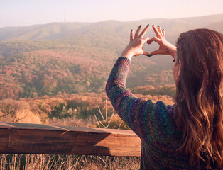 Woman making heart with her hands showing gratitude to nature and life. Happiness concept.